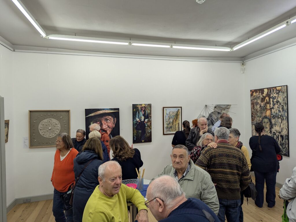 In Galerieräumen mit weißen Wänden stehen jede Menge Menschen und betrachten die ausgestellten Bilder.